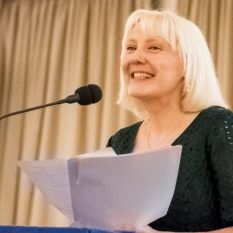 Headshot of Tressa Burke who has blond shoulder length hair, wearing a green dress and holding papers, standing at a microphone. Headshot of Tressa Burke who has blond shoulder length hair, wearing a green dress and holding papers, standing at a microphone.