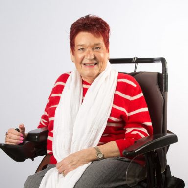 Portrait of GDA's treasurer Morag Mackay. Morag has short red hair, is wearing a red and white stripy top and a white scarf, and is sitting, smiling, with her hand on the arm of her powered wheelchair. Portrait of GDA's treasurer Morag Mackay. Morag has short red hair, is wearing a red and white stripy top and a white scarf, and is sitting, smiling, with her hand on the arm of her powered wheelchair.