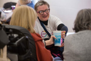 A member in a GDA t-shirt passes a cup to another member at a Drivers for Change meeting