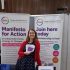 Ruth from GDA, grinning behind an information stall, with GDA pop up banners leaflets and information.