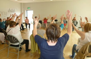 Members are seated and all raise their hands, sitting in a circle.