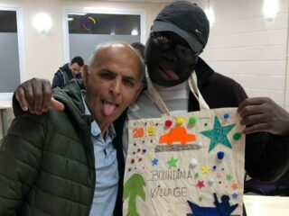 two GDA members arm in arm stick out their tongues and show off their colourful craft work - a tote bag personalised and decorated