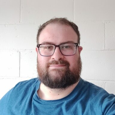 Kevin has short hair, dark rimmed glasses and a full beard. He's wearing a blue tshirt. Kevin has short hair, dark rimmed glasses and a full beard. He's wearing a blue tshirt.