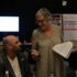 Pennie Taylor, Chair of the hustings, holds a microphone infront of a member who is asking a question at the hustings.