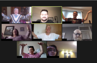 GDA members on Zoom are sat at the centre of their screens with their arms raised horizontal and bent at the elbow so that the forearm points upwards. The hands are then stretched horizontal away from the body, creating a Tai Chi pose