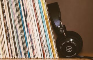 A close up on a stack of music LPs standing and slighly leaning to the side. A set of black headphones rests against them.