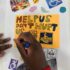 GDA members hand is in frame, drawing a poster that reads 'Help us don't hurt us'. The poster is brightly coloured, with collage cut outs of disabled signs, of transport and images of people in a wheelchair.