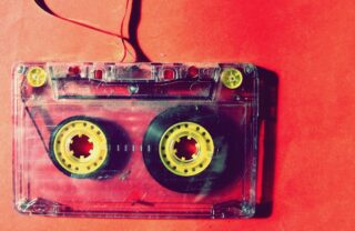 a cassette tape sits on a red table, the close up image of the cassette shows the tape spilling out in a loop shape outside the cassette.