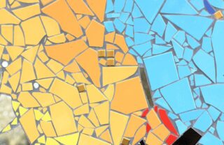 a mosaic art piece takes up the entire image, with triangular and unusually shaped mosaic pieces that start off yellow on the left and blend to orange. half way across the piece the mosaics change to light blue and there is a small black section at the bottom right.