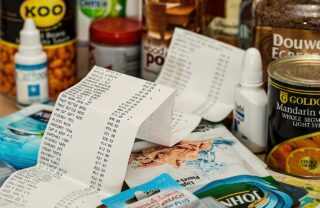 a shopping list is laid out, unfolded on a table containing numerous canned goods and other grocery shopping items.
