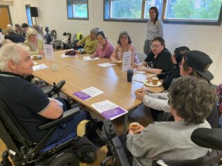 The photograph shows several GDA members sitting around a large table. At the far end of the table is Patricia Ferguson, MP for Glasgow West. She is listening to one of the GDA members at the other end of the table who is talking.