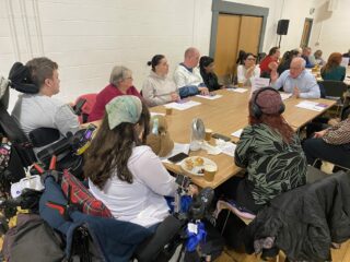 The photograph shows several GDA members sitting around a large table. At the far end of the table is Martin Rhodes, MP for Glasgow North. The group are in discussion.